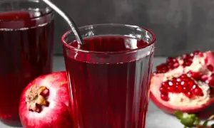 Szklanka z sokiem z granatów, obok owoców. Czy sok malinowy obniża ciśnienie? Ten napój może pomóc.