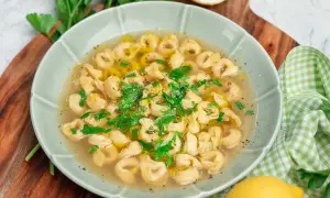 En skål med tortellini in brodo, garnerad med färsk persilja och en citronskiva.