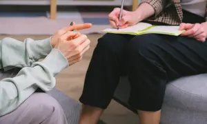 Rozmowa terapeutyczna o uzależnieniach behawioralnych. Jedna osoba mówi, druga notuje.
