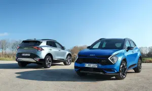 Dwa Kia Sportage GT Line: jeden niebieski z przodu, drugi srebrny z tyłu, na tle błękitnego nieba i drzew.