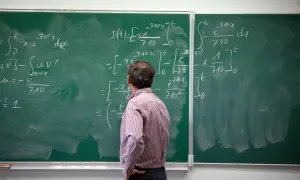 Nauczyciel rozwiązuje skomplikowane równania na tablicy. Jego pensum obejmuje analizę matematyczną.
