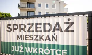 Baner z napisem "SPRZEDAŻ MIESZKAŃ JUŻ WKRÓTCE" na tle nowoczesnego budynku mieszkalnego.