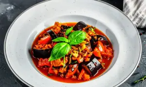 Un plat de ratatouille au four, garni de basilic frais, avec des aubergines, des tomates et d'autres légumes mijotés dans une sauce savoureuse.