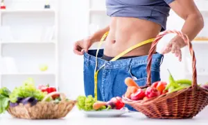 Uomo con jeans larghi e metro, simbolo di successo con dieta ipocalorica. Cesti di verdura fresca in primo piano.