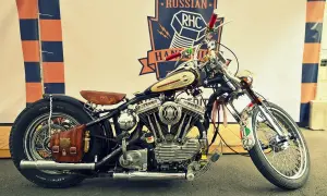 Customowy motocykl z chromowanymi elementami, skórzanym siedzeniem i sakwą, na tle baneru Russian RHC.