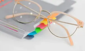 Okulary korekcyjne na stosie notatników z kolorowymi zakładkami.