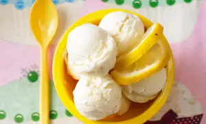 Erfrischendes Buttermilch Zitronen Eis in einer gelben Schale, garniert mit Zitronenscheiben. Eine gelbe Löffel liegt daneben.