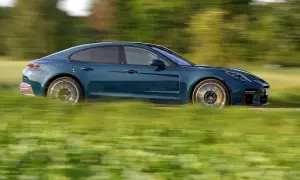 Niebieski Porsche Panamera Turbo S pędzi przez zielone pole, rozmazując krajobraz.