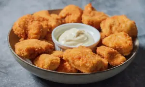 En skål med gyllene, krispiga chicken nuggets och en liten skål med krämig dipp. Perfekt för en snabb och god måltid.