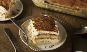 Une part de tiramisu, dessert dont l'origine est débattue, sur une assiette avec une fourchette. Le dessert est saupoudré de cacao.