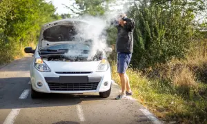 Mężczyzna z rozpaczą w rękach przy białym samochodzie, z którego bucha para. Rozbiegany diesel na poboczu drogi.