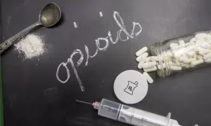 Napis "opiaty" na tablicy, obok łyżki z proszkiem, strzykawki i butelki z tabletkami.