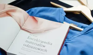 Książka "Encyklopedia materiałów odzieżowych" leży na niebieskiej i czarnej tkaninie. Może zawierać informacje o wadach wiskozy.