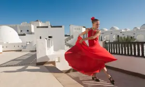 Bailarina con vestido rojo gira con gracia, evocando la pasión de los flamencos de Jerez bajo un cielo azul.