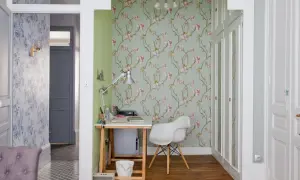 Un pan de mur de salon est habillé d'un papier peint floral aux fleurs roses sur fond vert pâle. Un bureau et une chaise blanche complètent l'espace.