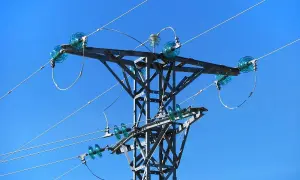Metalowa konstrukcja słupa energetycznego z niebieskimi izolatorami, przez które biegnie linia średniego napięcia.