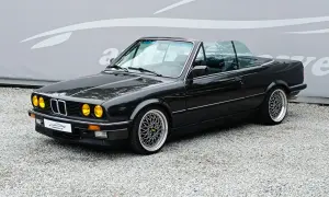 Czarny kabriolet BMW E30 z żółtymi światłami i felgami BBS. Klasyk na drodze.