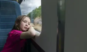 Zamyślona dziewczynka w różowej bluzce patrzy przez okno pociągu. Czy dziecko może samo jechać pociągiem?