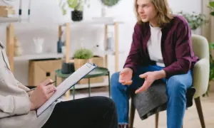 Rozmowa z psychologiem. Mężczyzna opowiada o swoich problemach, a psycholog notuje. Jak wybrać psychologa? Zaufanie i komfort to klucz.