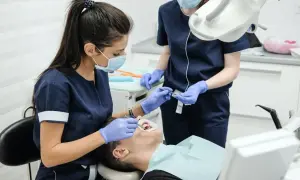 Dwie dentystki w maseczkach i rękawiczkach wykonują zabieg u pacjenta.