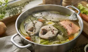 Un poisson entier et des darnes de poisson cuisent dans un court-bouillon avec des légumes et des herbes.