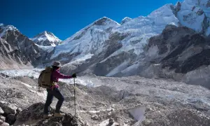 Turystka z plecakiem i kijkami trekkingowymi podziwia majestatyczne szczyty Himalajów w okolicy **Mount Everest Base Camp**.
