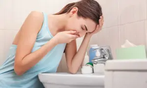 Kvinna med handen för munnen, böjd över ett handfat, upplever illamående sent i graviditeten.