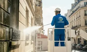 Un ouvrier en nacelle effectue le nettoyage mur extérieur d'un immeuble parisien avec un nettoyeur haute pression.