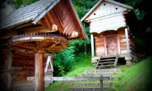 Drewniane chaty w skansenie, przypominające architekturę Kurpiów, z widocznym kołem młyńskim.