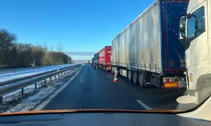 Longue file de véhicules poids lourds à l'arrêt sur une autoroute enneigée sous un ciel bleu clair.