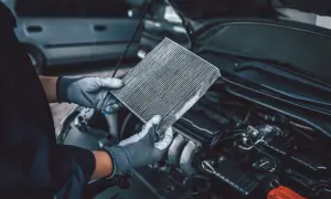 Mains gantées tenant un filtre à air encrassé, expliquant pourquoi changer filtre a air pour une meilleure performance moteur.
