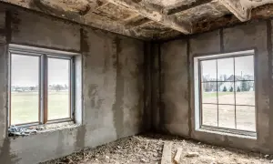 Niedokończony pokój z dwoma oknami. Widać gruz na podłodze i surowe ściany. Odległość okna od granicy działki i zgoda sąsiada to kluczowe kwestie przy budowie.
