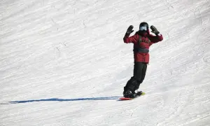 Snowboardzista w czerwonej kurtce z radością zjeżdża po stoku. Zastanawiasz się, ile kosztuje snowboard?