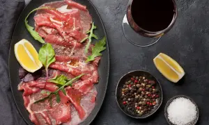 Delicioso carpaccio de ternera con rúcula, limón y pimienta. Acompañado de una copa de vino tinto.