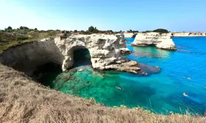 Scogliere bianche e mare cristallino nel Salento, con persone che nuotano e si godono il sole.