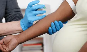 Blodprov tas för nipt test vecka 10. En hand med blå handske håller armen medan en annan hand med blå handske för in en nål.