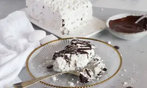 Una fetta di meringata al cioccolato, soffice e golosa, con scaglie di cioccolato e una cascata di salsa al cacao.