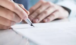 Dłoń pisze piórem na dokumencie. Czy CV musi być podpisane? To pytanie, na które odpowiedź znajdziesz w tym obrazie.
