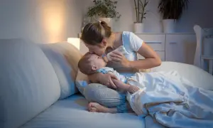 Matka karmi dziecko butelką w łóżku, czule całując je w czoło. Nawet koszmary senne nie są straszne, gdy czuwa kochająca mama.