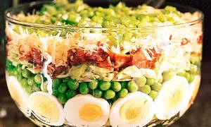 Lager på lager i en glasskål: ägg, gröna ärtor, sallad, bacon, ost och paprika. Ett härligt sallad recept!