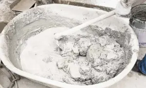 Mieszanie zaprawy z wapna palonego w dużej misie. Ręka w rękawiczce miesza gęstą, szarą masę.
