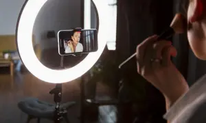 Idealne światło do makijażu: ring light oświetla twarz kobiety nagrywającej tutorial na telefonie.