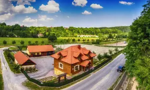 Drewniane budynki rancza z czerwonymi dachami, otoczone zielenią, pod błękitnym niebem z chmurami.