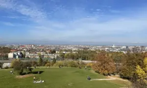 Widok na Kraków z zielonego wzgórza, gdzie ludzie odpoczywają. W oddali rozciąga się panorama miasta, a jesienne drzewa dodają uroku. To idealne miejsce na spacer, jak na **Kopcu Kraka**.