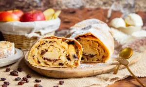 Ein köstlicher Apfelstrudel, wie ihn Landfrauen backen, mit saftiger Füllung und Puderzucker bestäubt. Dazu passen Rosinen und eine Kugel Eis.