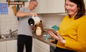 Mann gießt Wasser ein, Frau schaut aufs Tablet. Sie planen ihren Wasserverbrauch für 3 Personen pro Monat in m³.