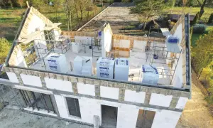 Budowa domu w toku. Widoczna ściana szczytowa z elementami konstrukcyjnymi i materiałami budowlanymi.
