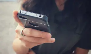 Dłoń z pierścionkiem trzyma telefon. Zastanawiasz się, dlaczego telefon wolno się ładuje? Może to wina kabla lub starej baterii.