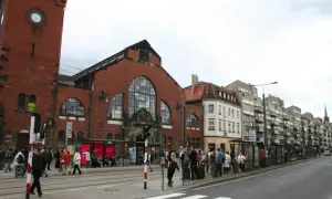 Menschen warten an einer Straßenbahnhaltestelle vor der imposanten Markthalle Breslau.