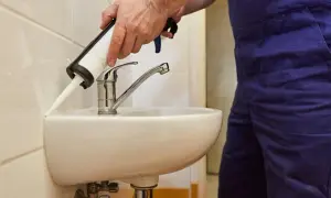 Ręce nakładają silikon wokół umywalki w łazience. Dowiedz się, jak wymienić silikony w łazience, aby zapewnić szczelność.